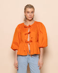 Model in een oranje blouse met pofmouwen en aan de voorkant drie strikjes